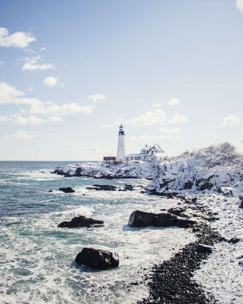 Maine Rocky Ocean Coast with white lighthouse in distance covered in snow